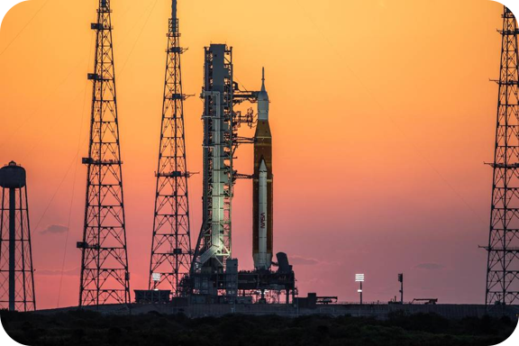 The sunrise casts a warm glow around the Artemis I Space Launch System (SLS) and Orion spacecraft.